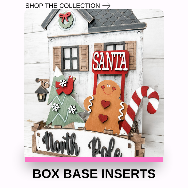 Christmas-themed decorative box base insert featuring a white house backdrop with a gingerbread man, Santa sign, tree, bird, lantern, candy cane, and a North Pole sign, with text reading SHOP THE COLLECTION and BOX BASE INSERTS.