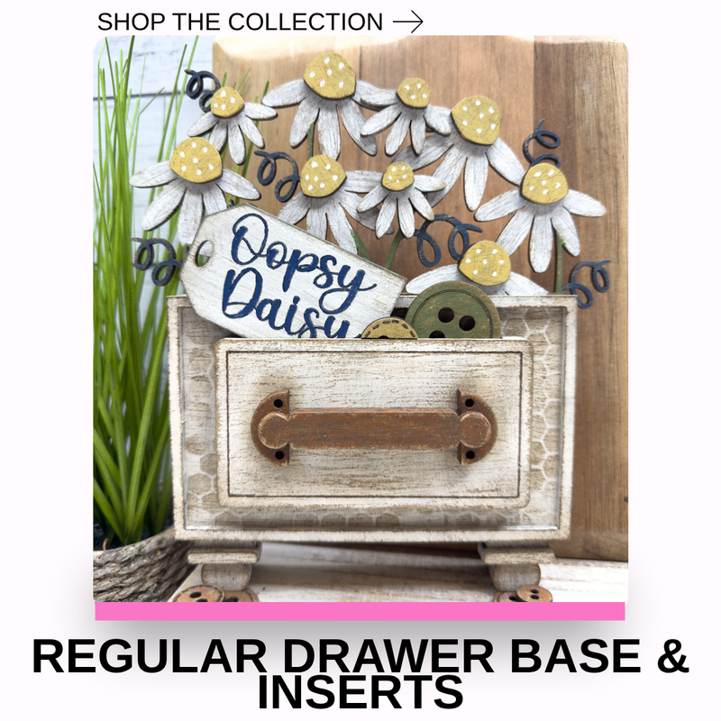 A decorative craft display featuring a distressed white drawer base with a brown handle, surrounded by layered daisy flowers in white and yellow, a sign reading 'Oopsy Daisy,' and a pink banner at the bottom with the text 'REGULAR DRAWER BASE & INSERTS.'.