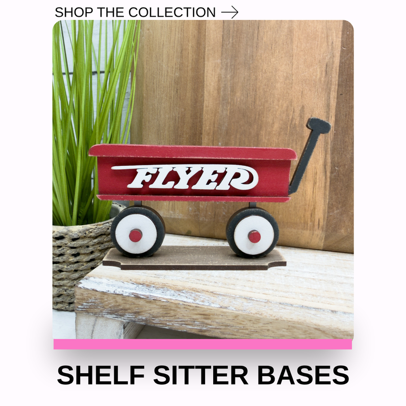 A red wooden wagon-style shelf sitter base with white 'FLYER' lettering and black wheels, displayed on a rustic wooden surface with a plant and wood panel background. Text at the top says 'SHOP THE COLLECTION ->' and text at the bottom says 'SHELF SITTER BASES'.