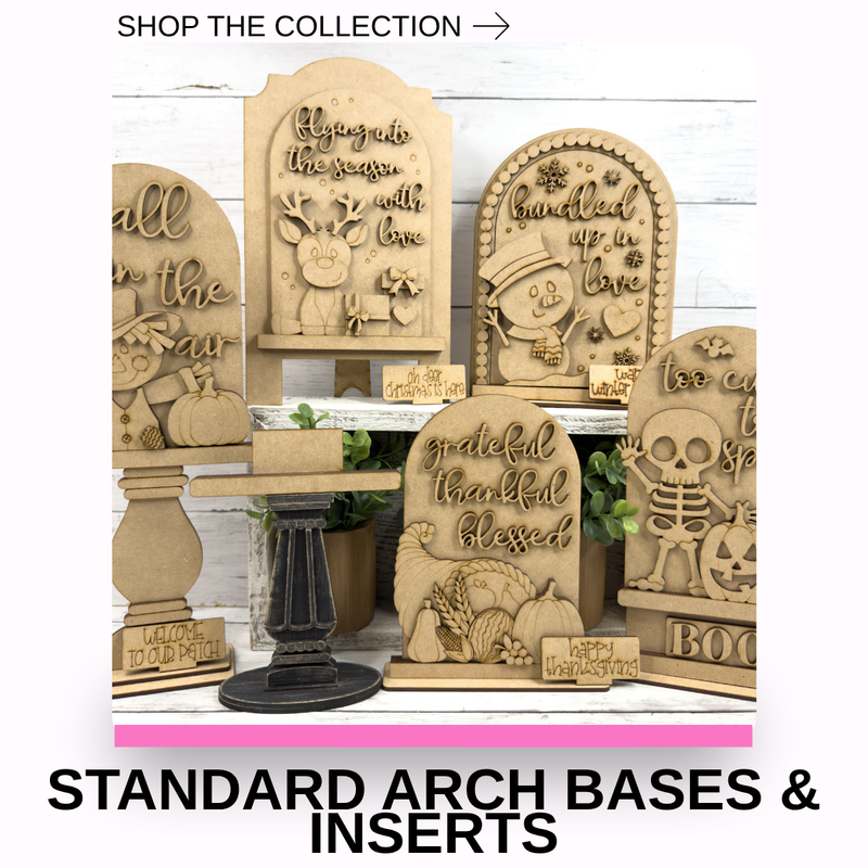 A display of carved wooden arch-shaped tombstone signs with Halloween-themed messages such as 'grateful thankful blessed,' 'happy Halloween,' 'boo,' and 'all in the world is worth living.' The signs are arranged on stands and pedestals against a white wood background, with text overlays reading 'SHOP THE COLLECTION' and 'STANDARD ARCH BASES & INSERTS.