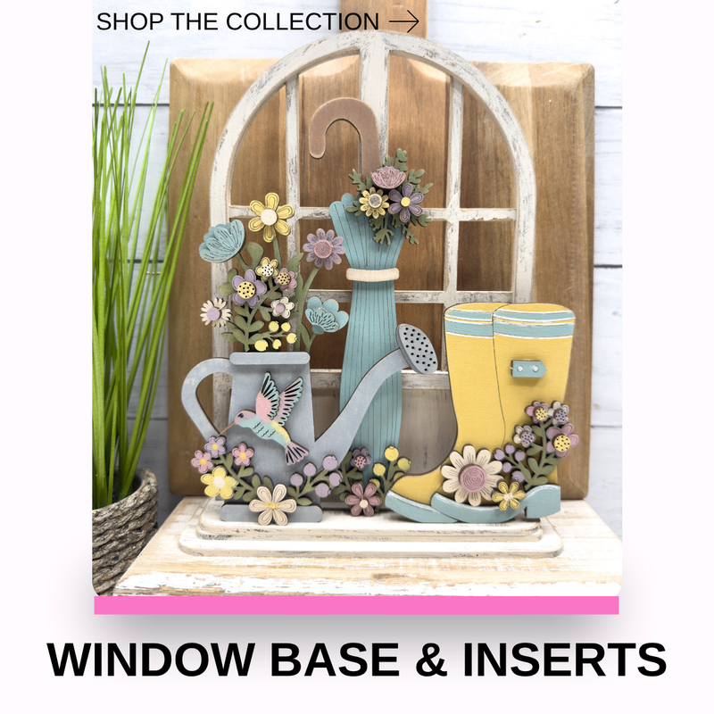 A decorative window-style display with gardening-themed inserts, including a gray watering can, blue vase with flowers, yellow rain boots, small flowers, and a bird figure, mounted on a rustic wood base. Text at the top reads 'SHOP THE COLLECTION →' and text at the bottom reads 'WINDOW BASE & INSERTS'.